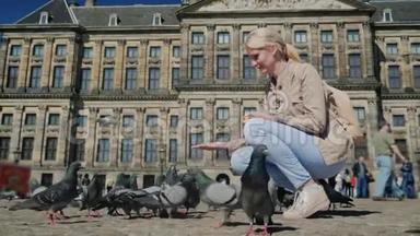 这位游客在阿姆斯特丹市中心皇家宫殿的背景下喂鸽子。 欧洲和旅游